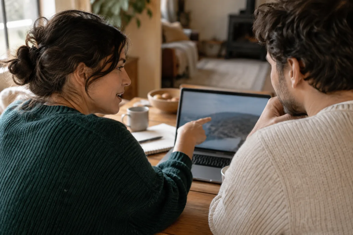 Two people at a kitchen table working through something together on a laptop